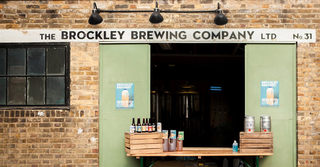 A table with bottles and kegs of beer laid out in front of Brockley Brewing Company door