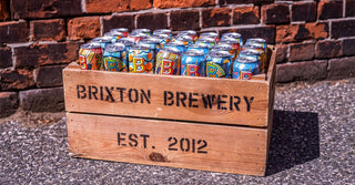 A wooden crate full of Brixton Brewery cans against a brick wall