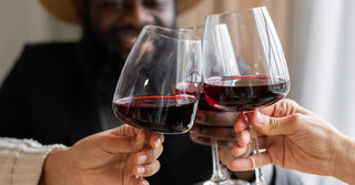Three large glasses of red wine are clinked with soft focus on a smiling man in the background