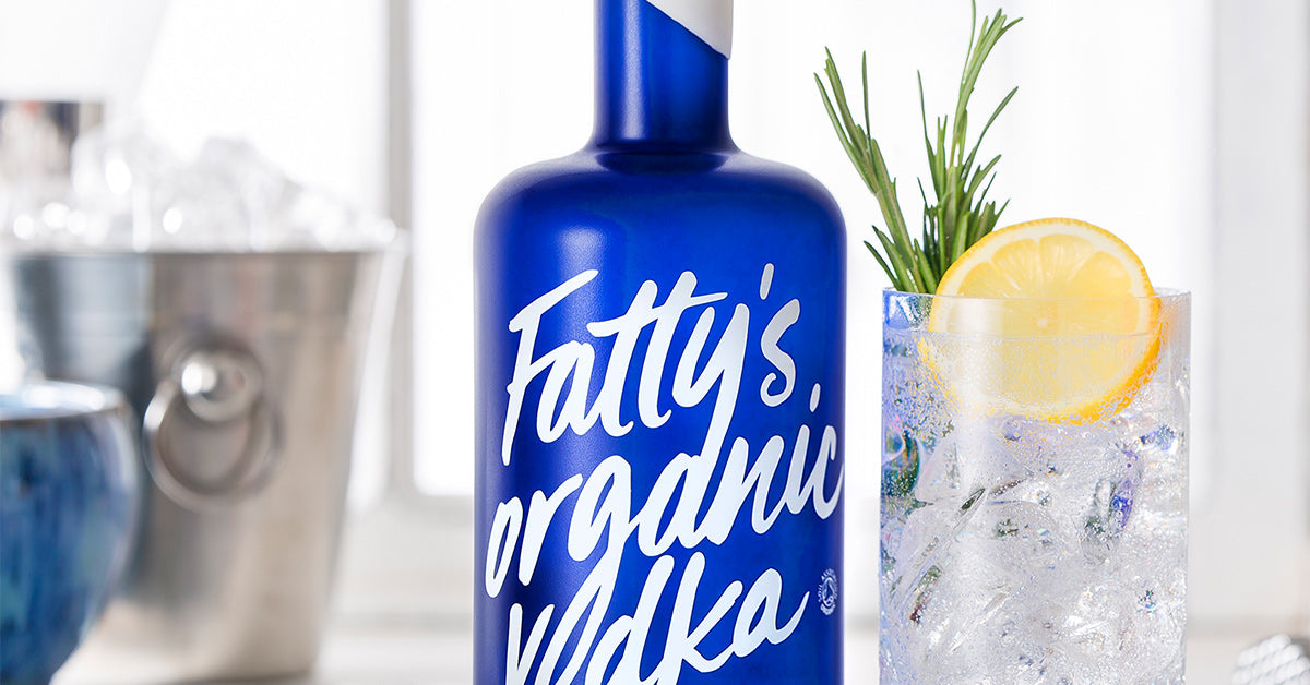 a blue and white bottle of Fatty's organic vodka next to a glass of vodka and tonic garnished with lemon and rosemary, a bucket of ice in the background
