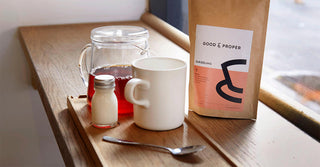 A pot of tea, a small milk bottle, a spoon, a white mug and a bag of loose leaf tea sit on a windowsill