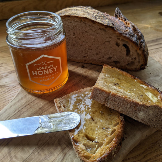 Jar of honey with a knife and slices of bread on a wooden board