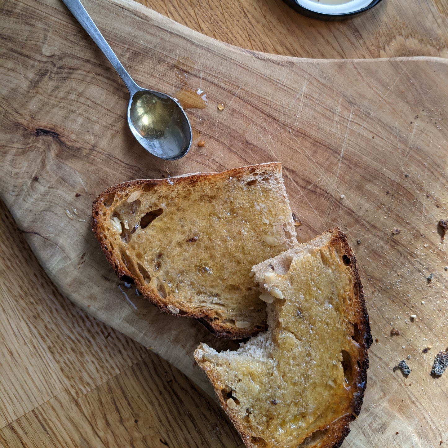Two pieces of toast on a wooden board with a honey spoon.