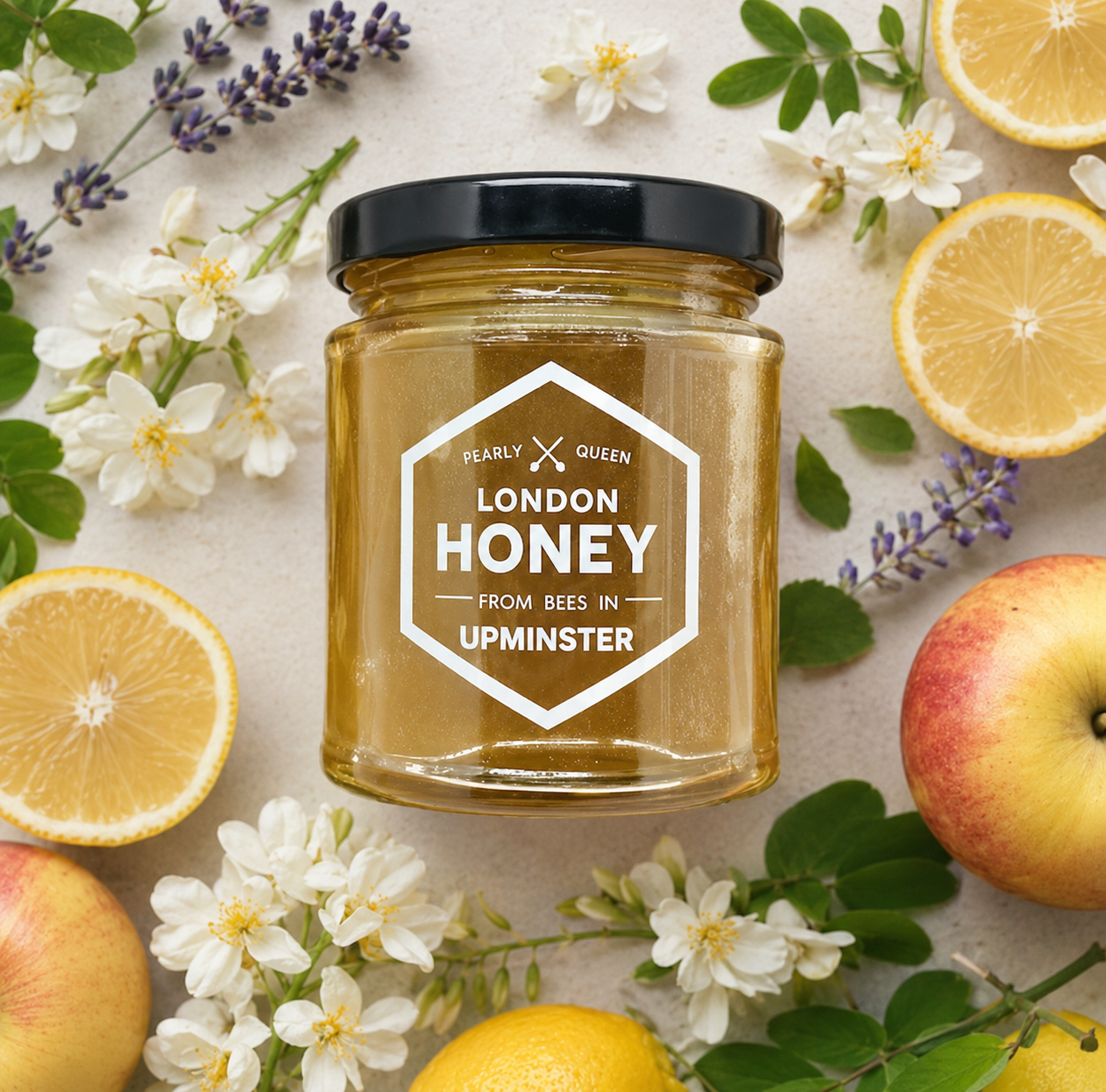 Jar of London Honey surrounded by lemons, apples, and flowers on a light background